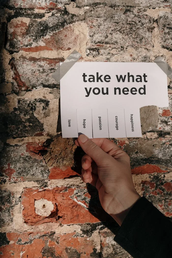 about-img A hand holding a paper note taped on a brick wall with motivational words to pick from.